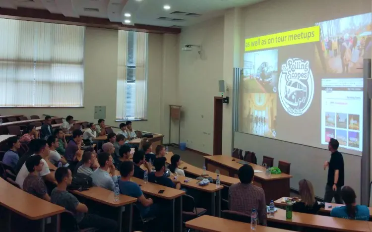 Lecture hall with attendees watching a presenter point to a screen about Rolling Scopes meetups